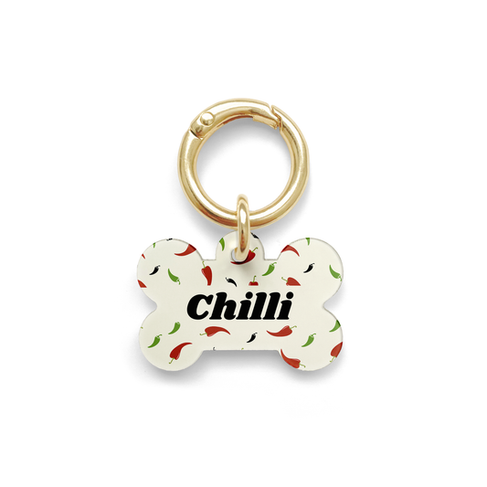 Custom pet ID tag with a design showing green red and black chillies on a bone shaped beige background with gold ring.
