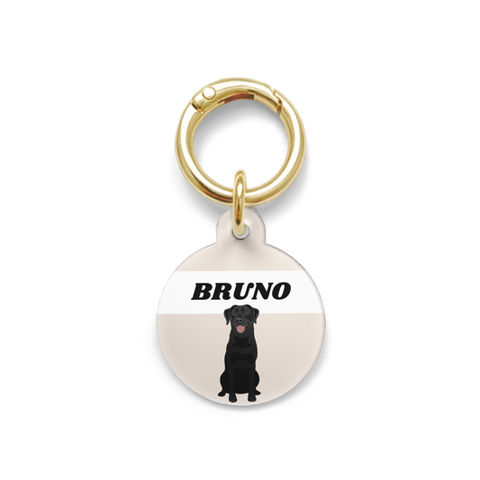 Black Labrador illustration on a circular dog ID tag with a beige background and gold ring.