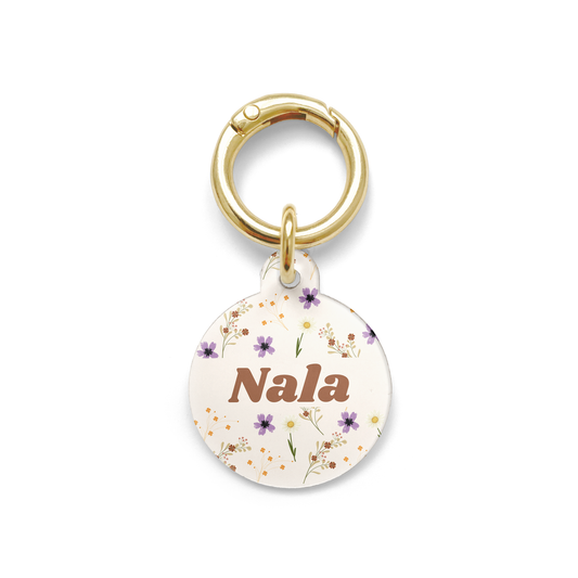 Floral pet ID tag with a design showing a range of purple, yellow and orange flowers on a beige background with gold ring.