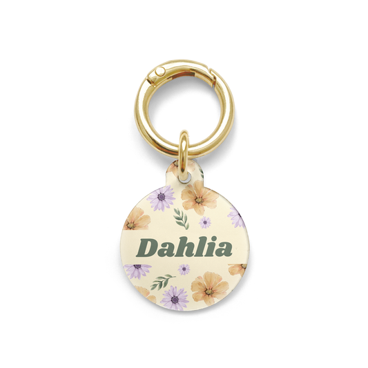 Summer flowers with purple and orange hues spread on a circular shaped pet ID tag with a gold ring.